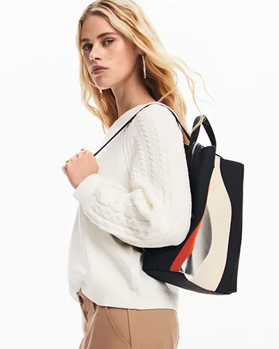 Woman in cream cable-knit jumper carrying a striped shoulder bag